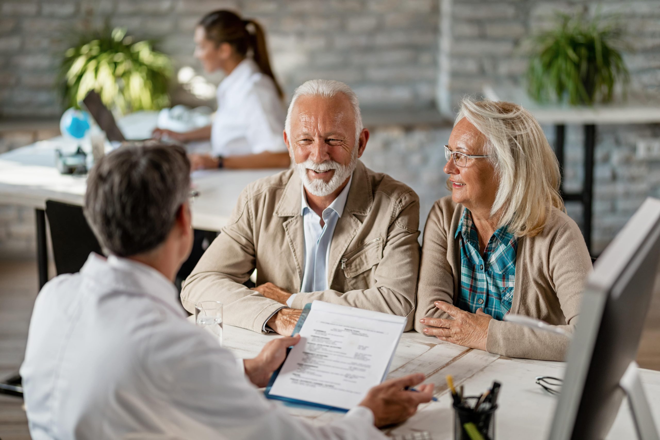 happy-senior-couple-communicating-with-doctor-about-their-health-insurance-while-going-through-paperwork-min